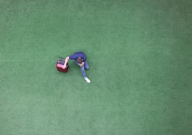 Photo sad man with suitcase sitting on green grass and holding his head top view