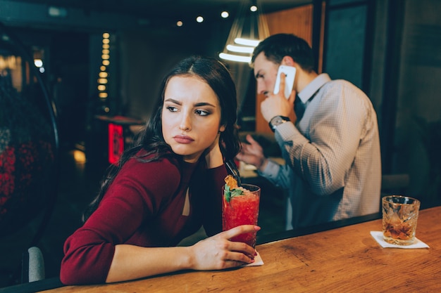 Foto triste di ragazza che guarda a destra. è triste perché l'uomo sta rispondendo alla telefonata e non sta trascorrendo del tempo con lei. non ha un buon umore.