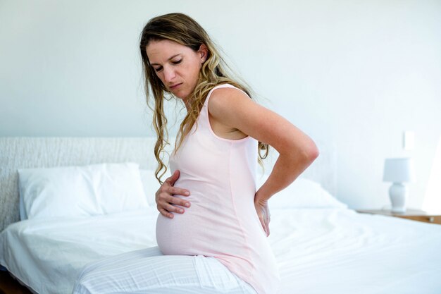 sad pregnant woman, sitting on a bed, with back pain