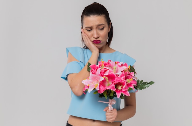 Sad pretty young woman holding and looking at bouquet of flowers