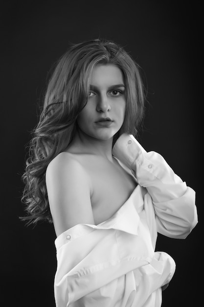 Sad romantic woman wears men's shirt posing in the shadows at studio. Black and white image