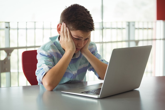 Грустный школьник смотрит на ноутбук в библиотеке