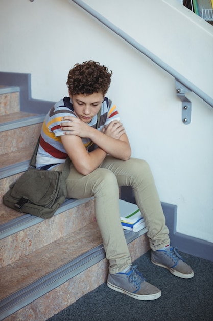 Photo sad schoolboy sitting alone on staircase