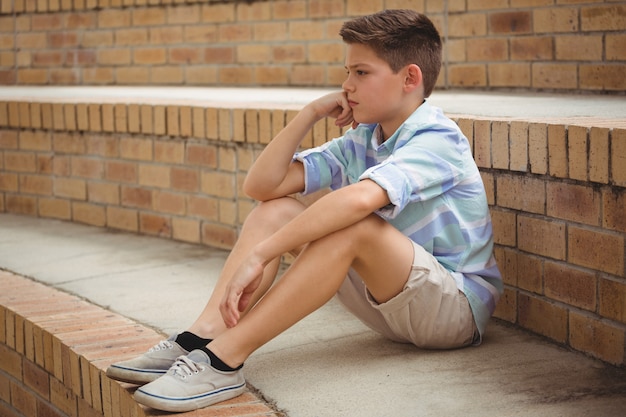 Sad schoolboy sitting alone on steps in campus