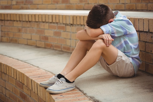 Foto scolaro triste che si siede da solo sui gradini nel campus