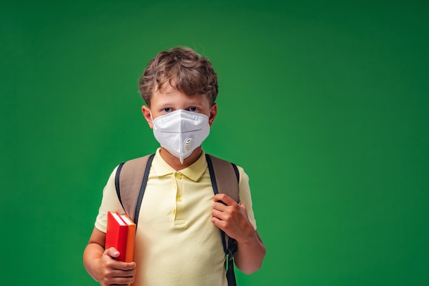 Sad schoolboy with a backpack and books in a protective mask