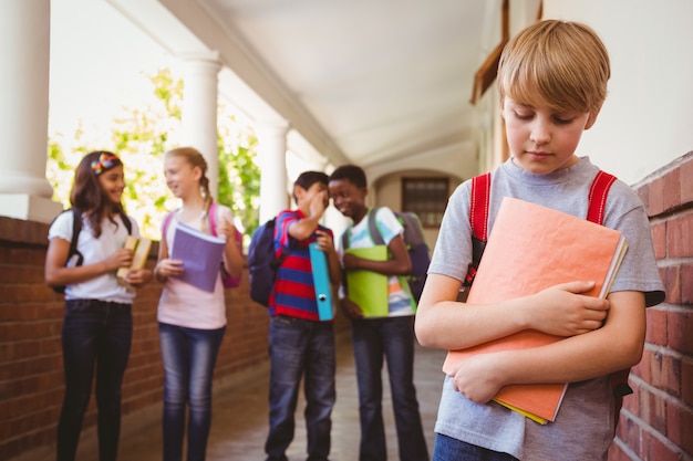 Sad schoolboy with friends in background at school corridor