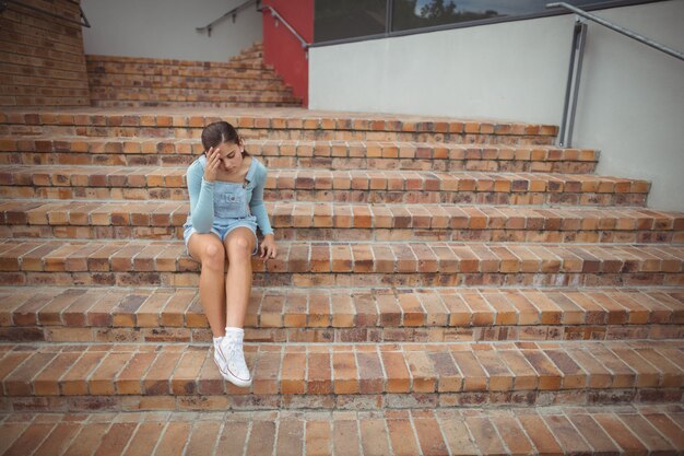 Photo sad schoolgirl sitting alone on staircase