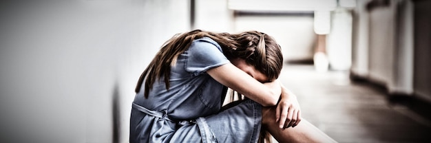 Sad schoolgirl sitting in corridor of school