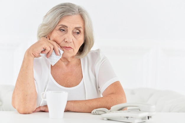 Donna anziana triste che si siede al tavolo con il telefono