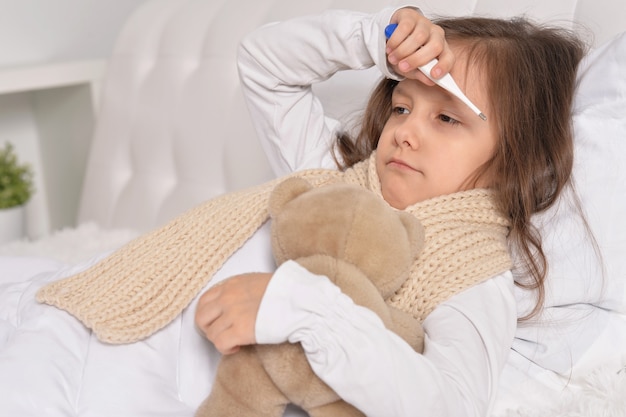 Photo sad sick little girl lying in the bed with teddy bear toy
