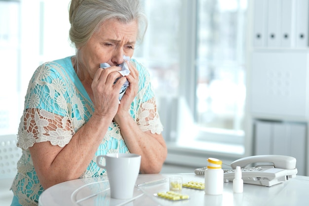 Sad sick senior woman sitting at table