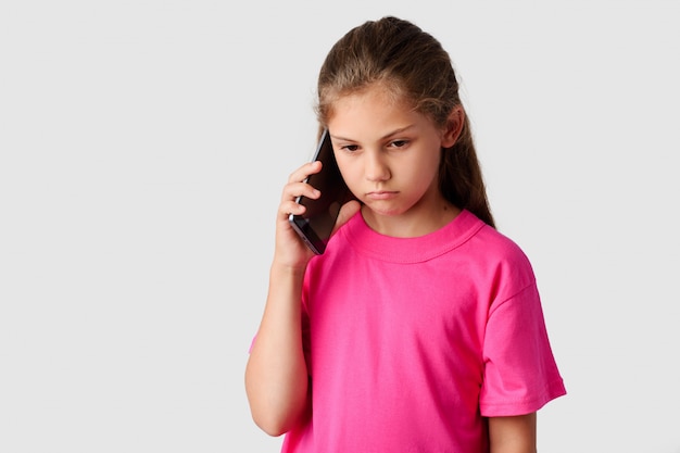 Piccola ragazza triste che parla sul telefono cellulare moderno