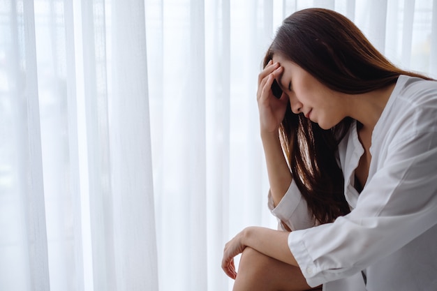 A sad and stressed young asian woman sitting alone in bedroom