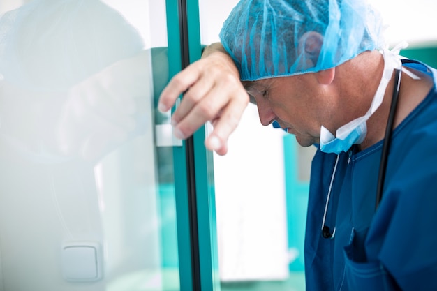 Sad surgeon leaning against the glass door