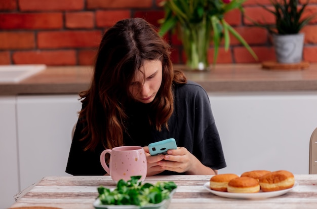 Sad teen girl uses a phone in the kitchen