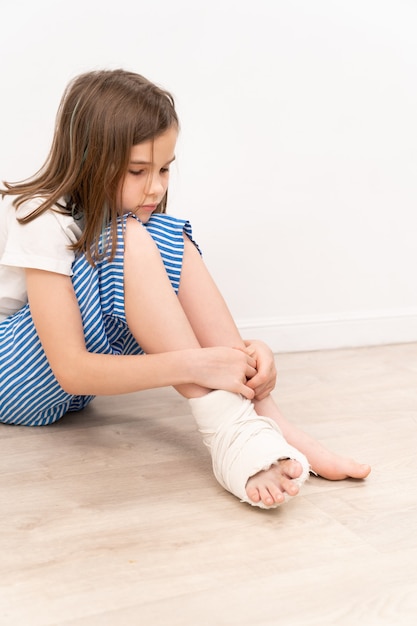 Sad teen girl with orthopedic plaster on her foot sitting on\
the floor. surgery to correct foot deformity in children.\
small-mobile patients.