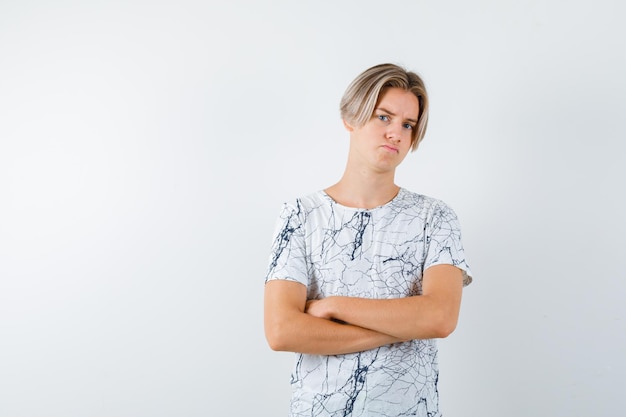 The sad teenage boy is looking at camera by crossing his arms on white background