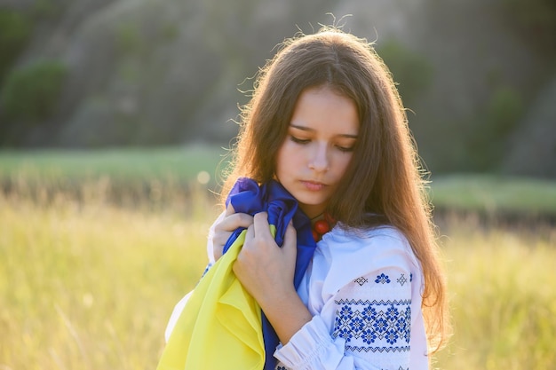 A sad teenage girl holds a Ukrainian flag to her chest