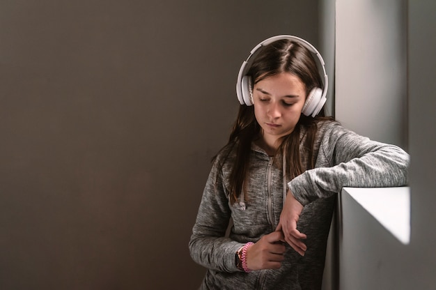 Sad teenage girl sitting on windowsill with earphones listening to music