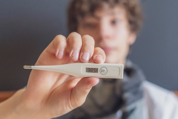 Sad teenager lay in bed and hold thermometer. illness concept b