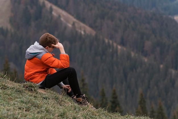 Sad teenager sits on hillside Boy resting in mountains Portrait of child in the autumn on hike