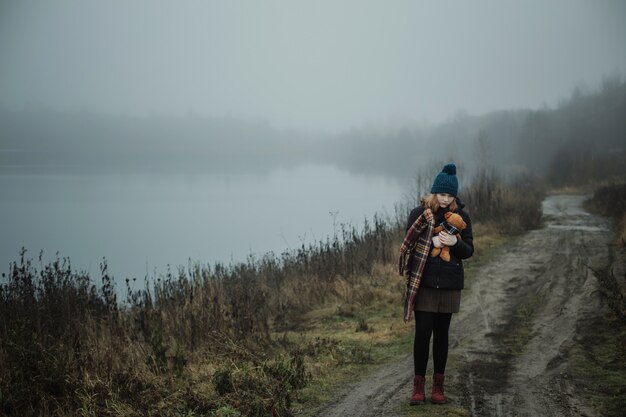 Sad teenager woman hugging teddy bear by foggy lake. concept of adolescence and adolescent problems.