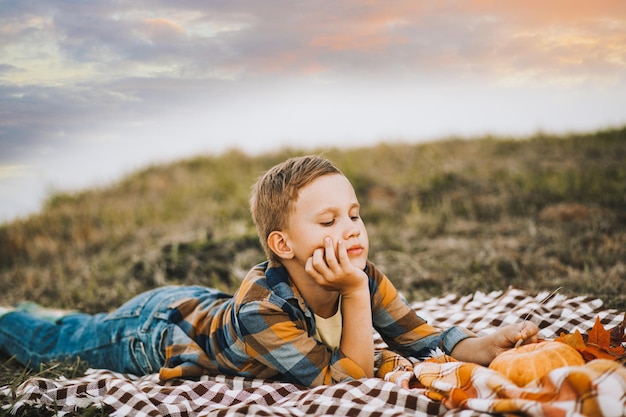 Sad thinking dreaming kid boy lies on a blanket near a river or lake