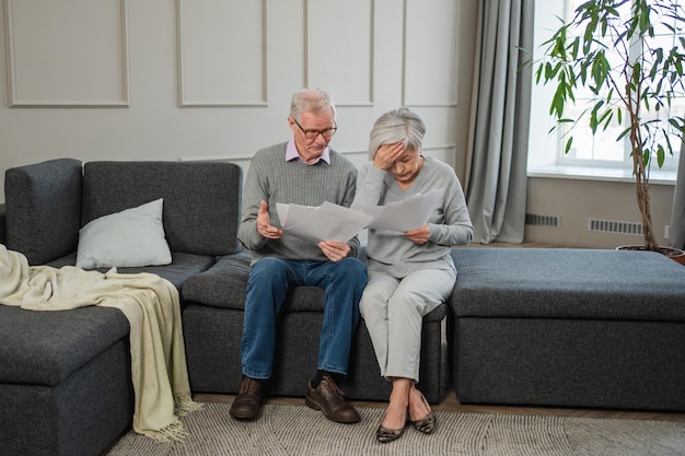 sad tired disappointed middle aged senior couple sit with paper document unhappy older mature man