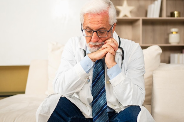 Sad tired mature senior male doctor in medical uniform in hospital or doctor office unhappy general