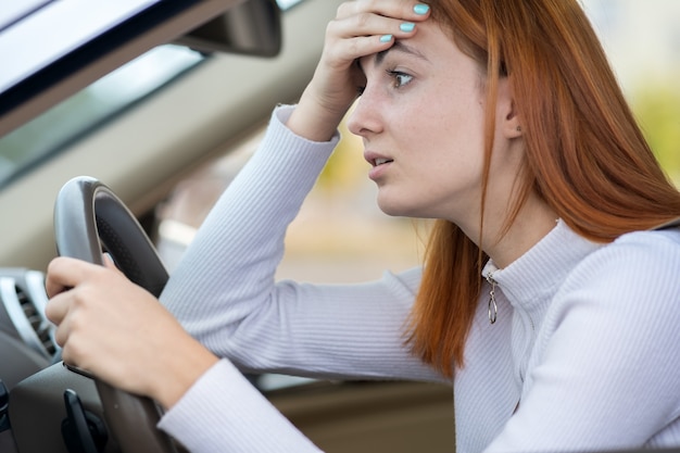 Sad tired yound woman driver sitting behind the car steering wheel in traffic jam.