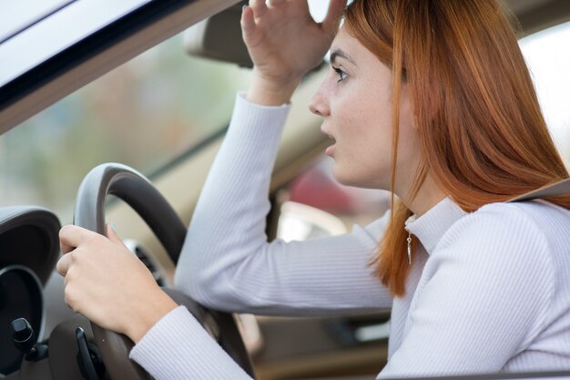 トラフィックの車のステアリングホイールの後ろに座って悲しい疲れている若い女性ドライバー