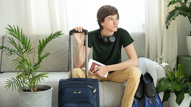 Sad tourist teen with a suitcase and flippers stays at home