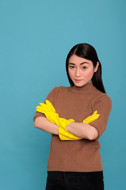 Sad unhappy and stressed asian housekeeper cross hand angry\
eyes with face expression wearing yellow gloves, cleaning home\
concept, tired frustrated female with negative state of mind