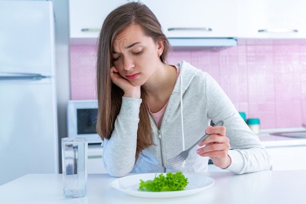 悲しい不幸な若い女性はダイエットにうんざりし、オーガニックで清潔な健康食品を食べたくない