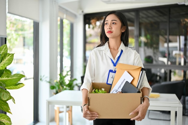 Sad and upset Asian female office worker carrying her belonging quitting a job being fired