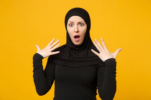 Triste sconvolto pianto confuso giovane donna musulmana araba in abiti neri hijab in posa isolata sulla parete gialla, ritratto. concetto di stile di vita dell'islam religioso della gente.