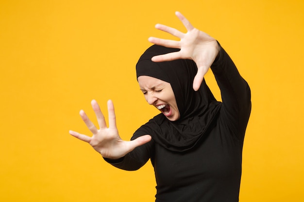 Sad upset crying confused young arabian muslim woman in hijab black clothes posing isolated on yellow wall  portrait. People religious Islam lifestyle concept. 