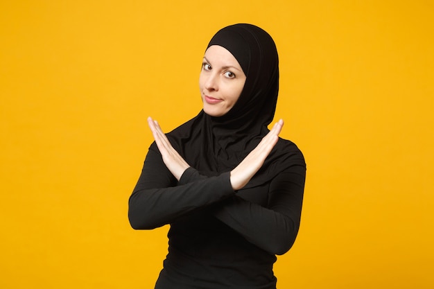 Sad upset crying confused young arabian muslim woman in hijab black clothes posing isolated on yellow wall  portrait. people religious islam lifestyle concept.