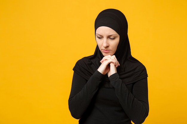 Triste sconvolto pianto confuso giovane donna musulmana araba in abiti neri hijab in posa isolata sulla parete gialla, ritratto. concetto di stile di vita dell'islam religioso della gente.