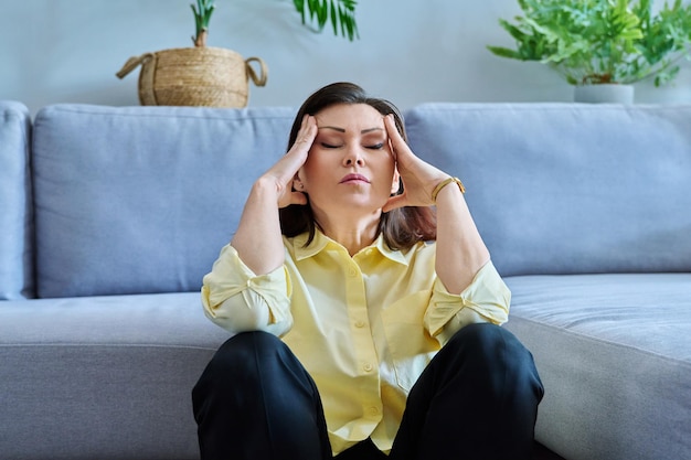 Sad upset middleaged woman sitting on the floor near the sofa