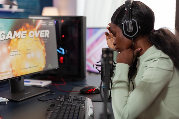 Sad upset woman gamer playing space shooter videogames losing online tournament while talking with players on streaming chat. Nervous streamer using RGB gaming computer. Game over on screen