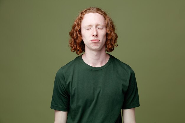 Sad with closed eyes young handsome guy wearing green t shirt isolated on green background