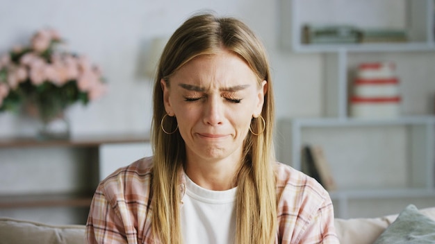 sad woman crying on the sofa at home with closed eyes