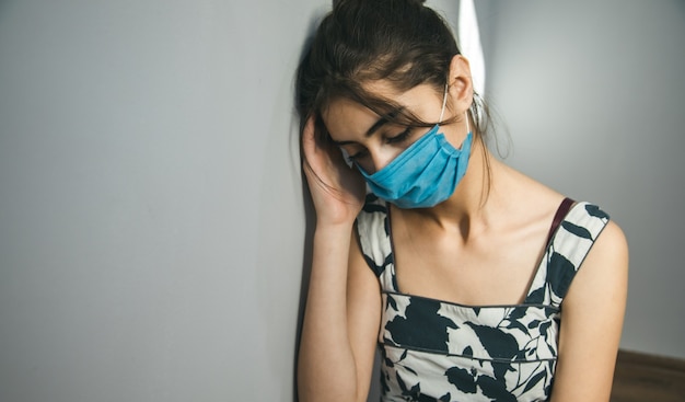 Sad woman face  mask on grey wall