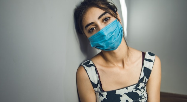 Sad woman face  mask on grey wall