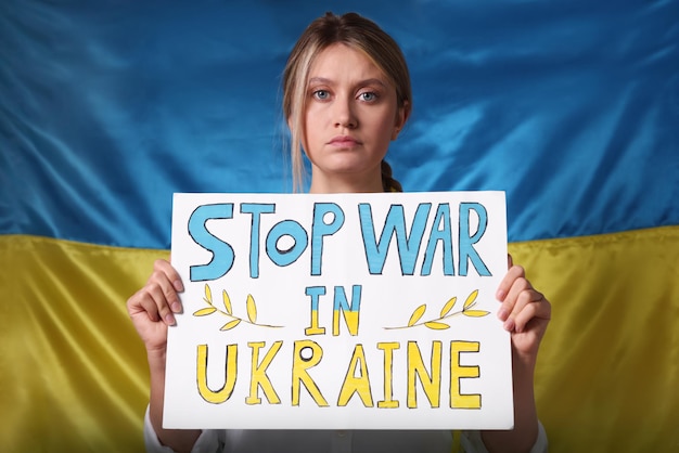 Foto triste donna con poster con parole stop war in ucraina vicino alla bandiera nazionale