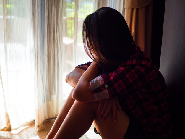 La donna triste abbraccia il suo ginocchio e piange. triste donna seduta da sola in una stanza vuota