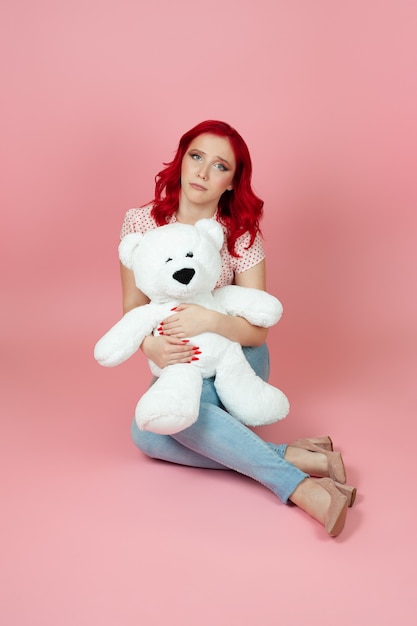 사진 빨간 머리를 가진 청바지에 슬픈 여자는 바닥에 앉아 큰 흰색 곰을 안아
