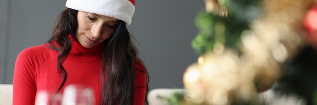 샴페인과 크리스마스 트리 두 잔 근처에 앉아 빨간 산타 클로스 모자에 슬픈 여자